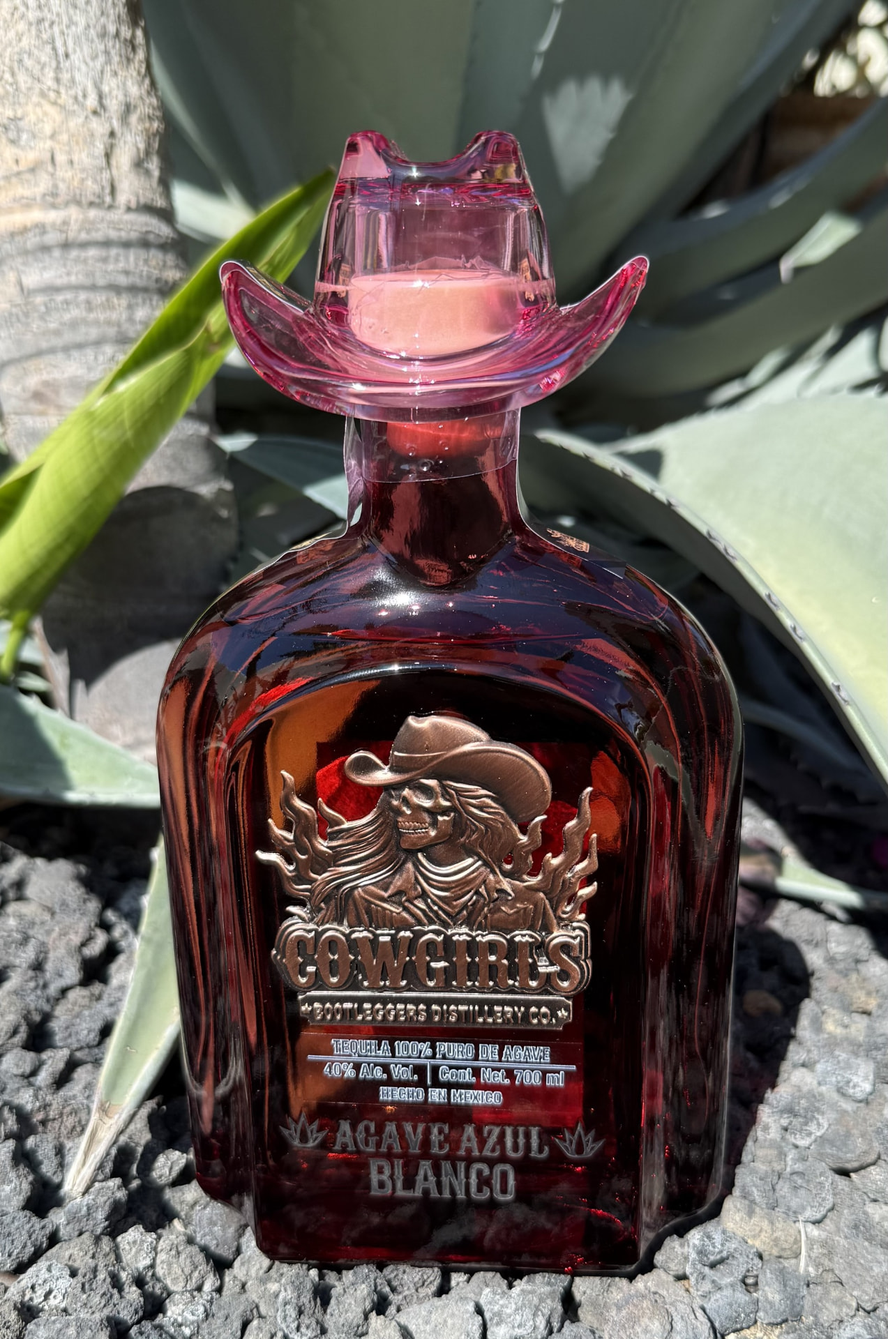 Rose-red Cowgirls Bootleggers Distillery Co. bottle with cowboy-hat stopper — Agave Azul Reposado